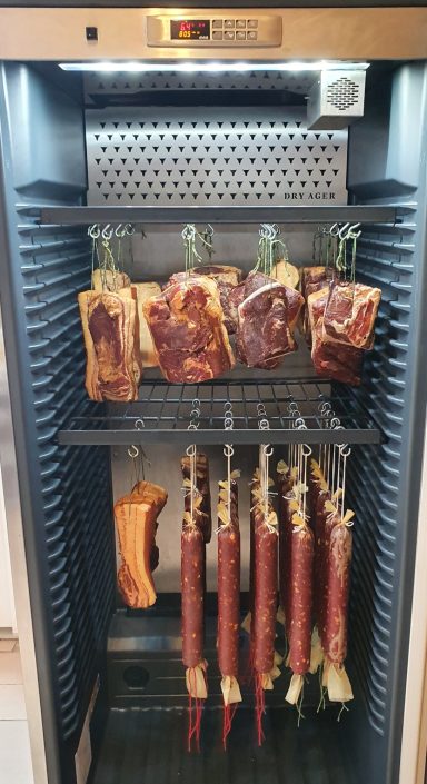 Eine verchromte Gerätschaft mit Trockenfleisch und Wurst zum Trocknen im Inneren.